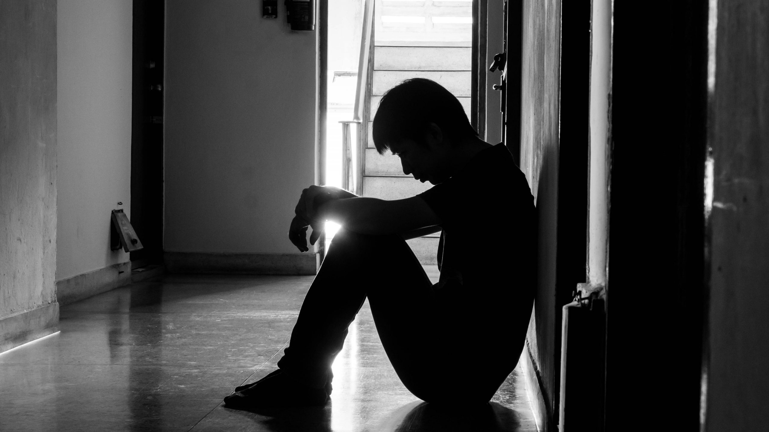 a sad young man sitting in the dark leaning against the wall with his ...